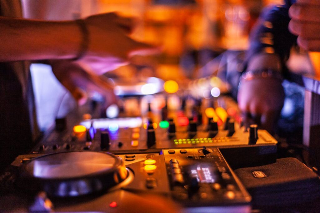 Close-up of DJ mixing console with hands adjusting controls at a lively nightclub.